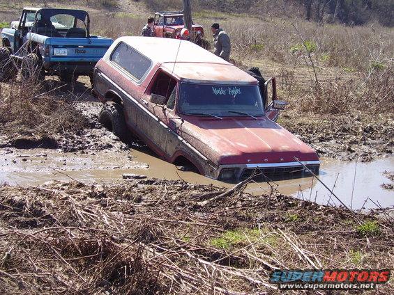 Red Ford Bronco stuck in mud, front grille visible, "Mother F***ers" sticker on windshield
