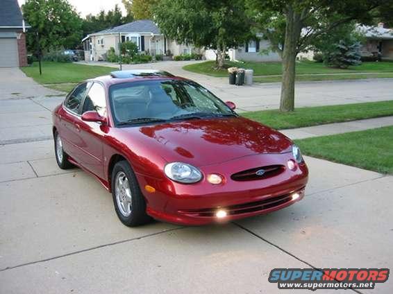 Red 1998 Ford Taurus sedan parked on a driveway, front 3/4 view