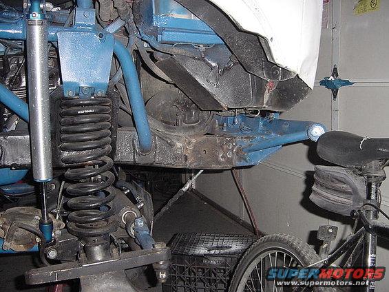 close-up of blue-painted off-road suspension components, shock absorber, and coil spring, with part of a bicycle visible