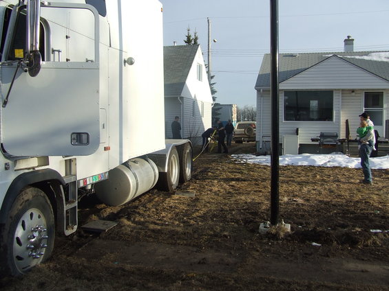 Semi-truck in foreground, white SUV in background with people near houses