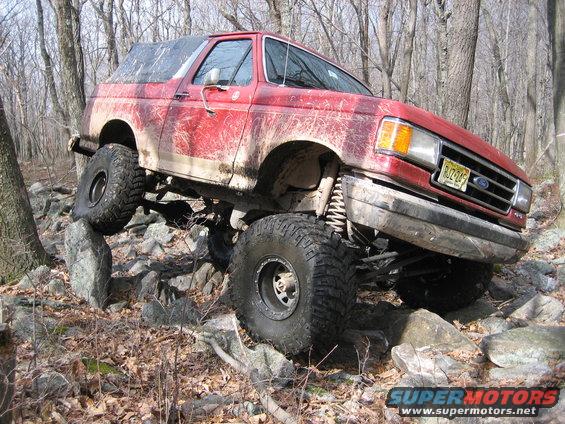 1990 Ford Bronco with lifted suspension and large tires navigating rocky terrain