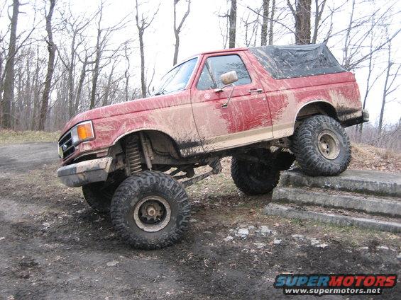 Red 1990 Ford Bronco climbing concrete steps, lifted with off-road tires