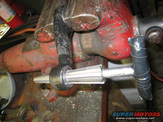 Steering linkage part held in a red vise, with a reamer tool inserted