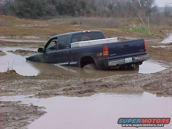 Dark blue pickup truck stuck in mud, side view. Silver toolbox in bed
