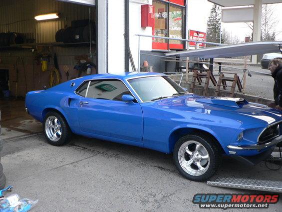 Blue 1969 Ford Mustang with a hood scoop and chrome wheels parked in a garage