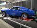 1969 Ford Mustang - A blue 1969 Ford Mustang is displayed on a black carpet with red support stands under the wheels.