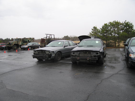 Two grey sedans with front ends removed, parked on wet asphalt