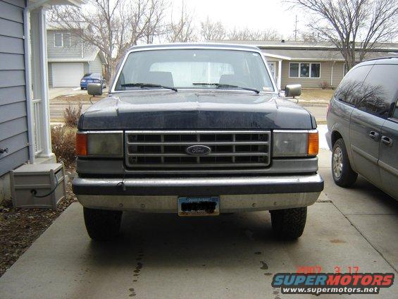 Dark blue Ford Bronco front view, parked in driveway. Chrome bumper, grille with Ford logo. License plate visible