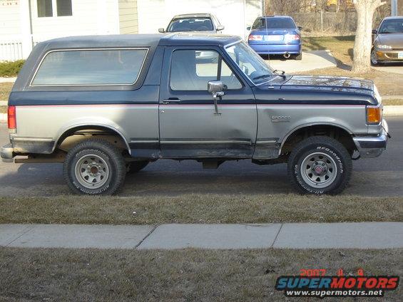 Side view of a two-tone Ford Bronco, silver and dark blue. It has a removable hardtop