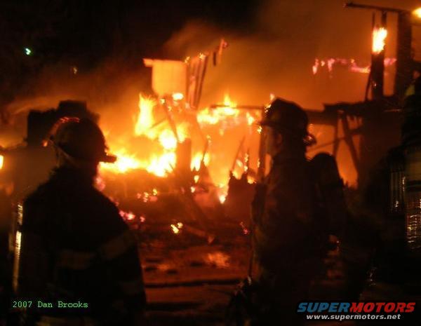 Firefighters in silhouette against a burning building at night
