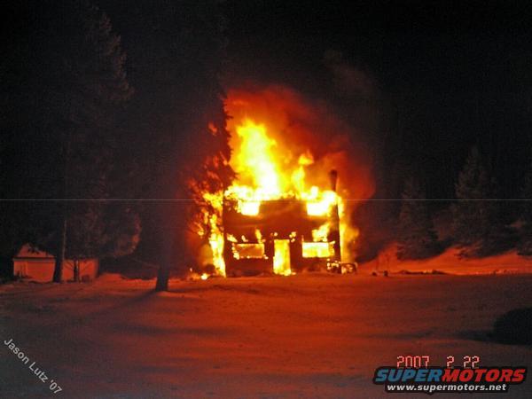 house engulfed in flames at night, snow on the ground, trees in background