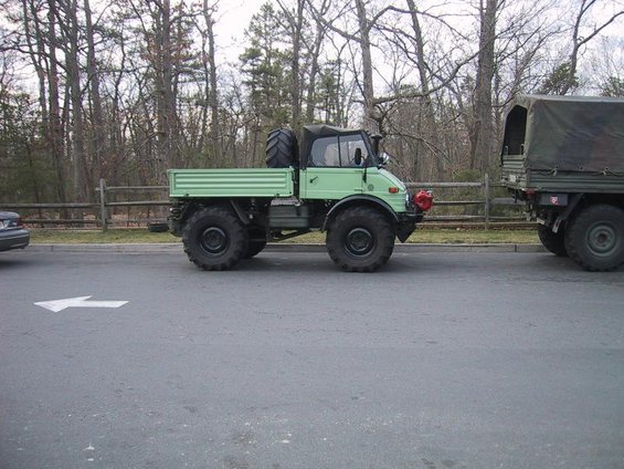 Green military truck with large tires and a spare tire on back, towing a camouflaged trailer