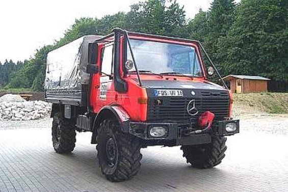 Red Mercedes-Benz Unimog truck with a tarped bed and large tires