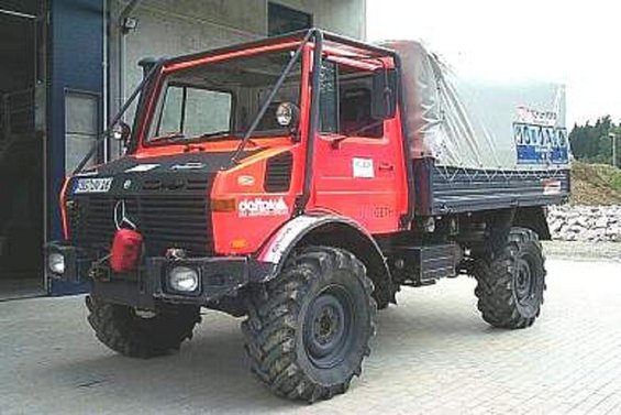 Red Unimog truck with a tarped bed parked outside a building