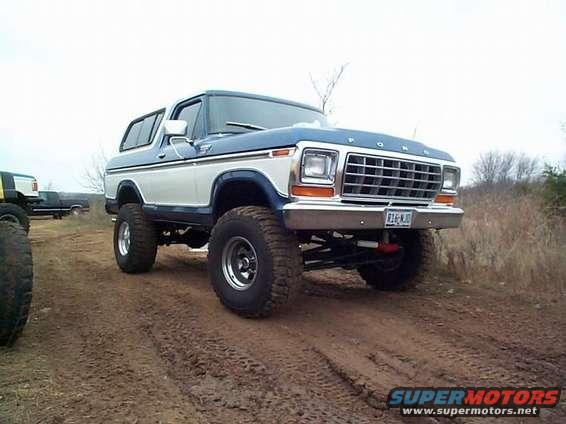 Blue and white 1978 Ford Bronco with lifted suspension and large tires on a dirt road