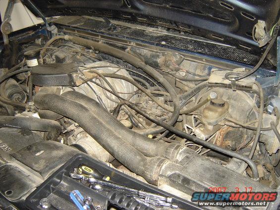 Engine bay of a 1988 Ford Bronco with hoses, wires, and a toolbox. The hood is open