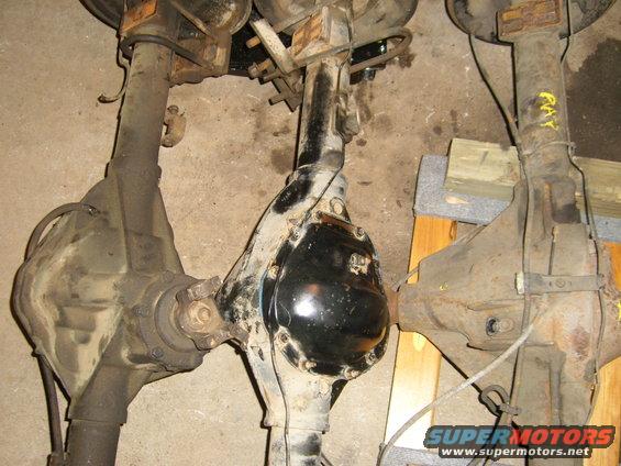 Three vehicle rear axles, one with a shiny black differential cover