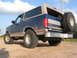 1996 Ford Bronco - Rear view of a blue 1996 Ford Bronco SUV with a tan top and a spare tire on the back.