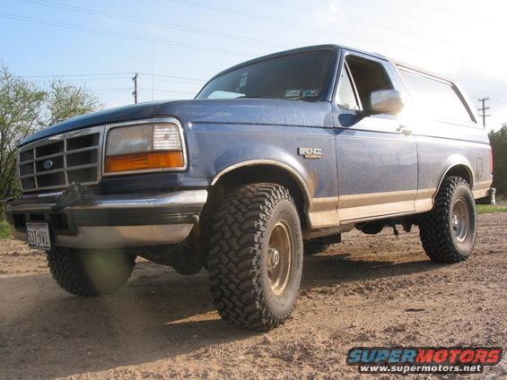 Blue 1996 Ford Bronco with tan stripe, lifted suspension, and off-road tires, viewed from the front 3/4 angle