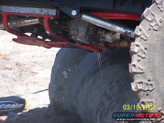Underside of a modified off-road vehicle with large tires and red suspension components. Water is dripping