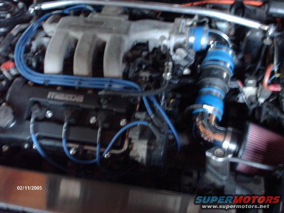 Engine bay showing a Mazda engine with blue spark plug wires and an aftermarket intake with a red air filter