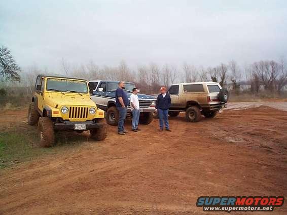 Yellow Jeep, blue Ford truck, and white Bronco parked on dirt with three men