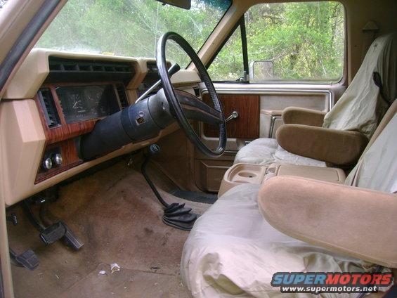 Interior view of a truck's dashboard, steering wheel, and front seats. Wood grain trim is visible