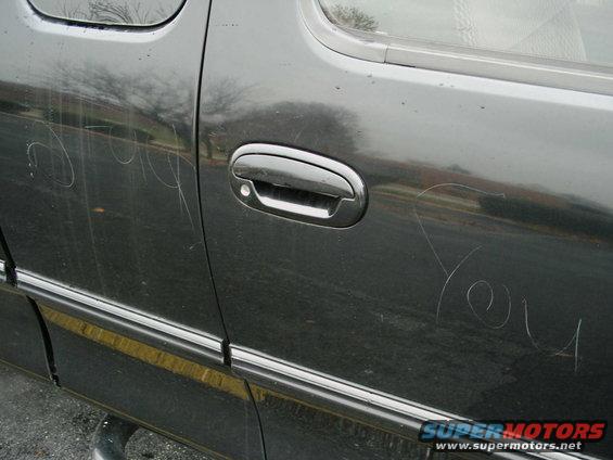 Dark truck door with scratches forming words, chrome handle, and trim