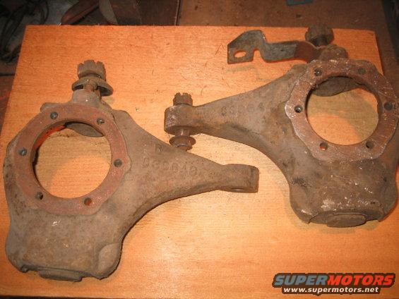 Two rusty steering knuckles with part numbers visible, resting on a wooden surface