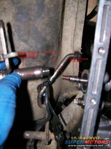 Close-up of a metal automotive part with red text annotations and a blue gloved hand