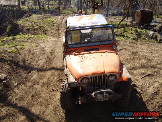 Orange off-road vehicle with a white roof sign driving on a dirt path