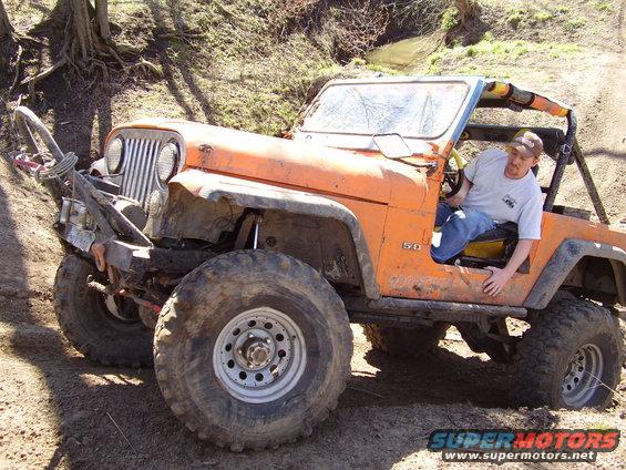 Orange Jeep CJ-5 modified for off-roading, with large tires and a winch. Driver is seated inside