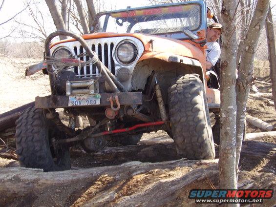 Orange Jeep CJ with large tires and winch on a wooded trail