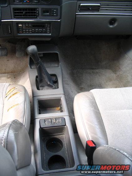 Car interior showing a torn passenger seat, center console with gear shifter, and dashboard with radio