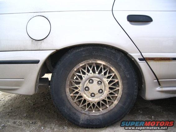Rear wheel and fender of a car, showing a gas cap door and a wire-spoke wheel