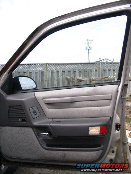 Interior of a car door showing the panel, window crank, and side mirror