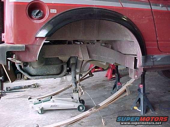 Red SUV rear suspension on jack stands, with a floor jack underneath