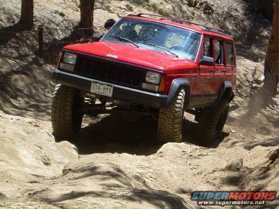Red 1996 Jeep Cherokee climbing a rocky, dirt trail with large tires