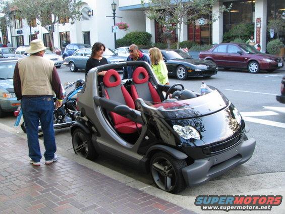 Black Smart Fortwo with red interior parked on a brick sidewalk
