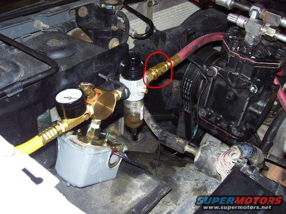 Engine compartment with air compressor, regulator, and gauge. Red circle highlights a brass fitting