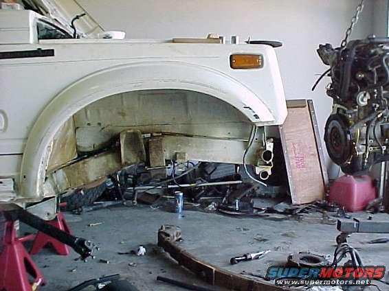 White SUV chassis on jack stands, engine removed, in a garage