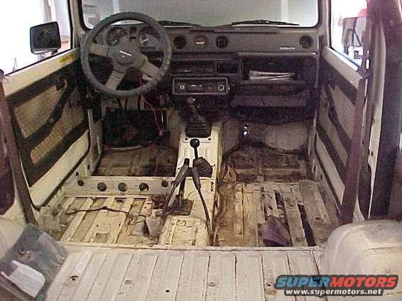 Interior of a white vehicle with removed seats and flooring, showing the transmission tunnel and dashboard