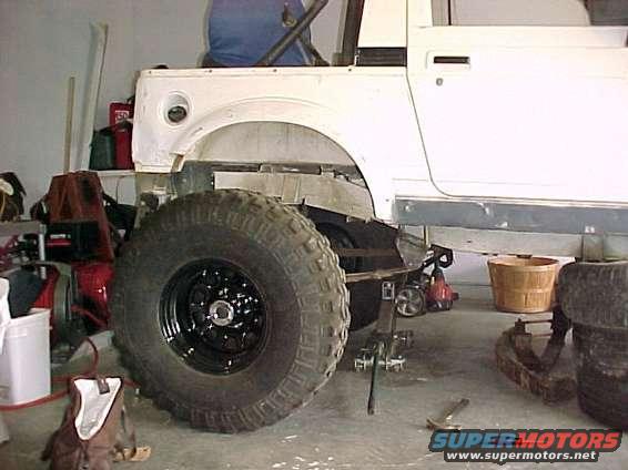 White SUV chassis with a large off-road tire on the left side, undergoing repairs