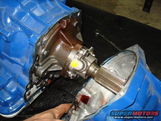 Blue transmission housing with rusty metal components and a splined shaft. A hand points to red fluid
