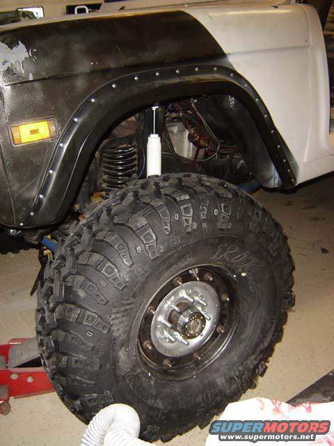 1971 Ford Bronco front fender and large off-road tire with custom wheel. The fender is black with rivets and a yellow turn signal