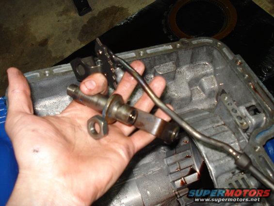 Hand holding a metal transmission component with a nut nearby, over an open transmission case