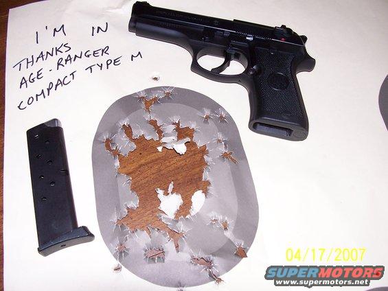 Black pistol and magazine next to a target with bullet holes
