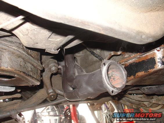 Close-up of black exhaust headers attached to an engine block, viewed from underneath a vehicle