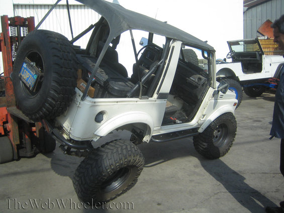 1987 Suzuki Samurai with soft top removed, lifted by forklift, another Jeep visible behind