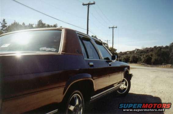 Maroon Ford Crown Victoria with chrome trim and aftermarket wheels parked on a dirt road